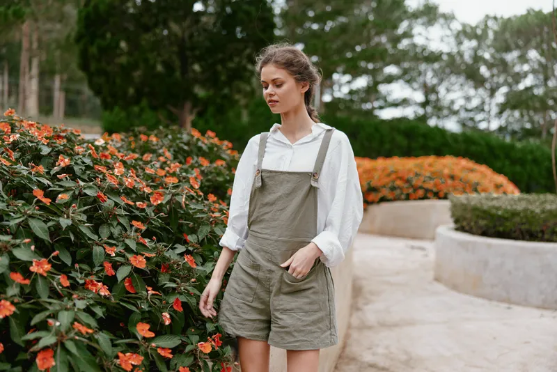 Young woman in a light outfit exploring a garden filled with vibrant flowers, evoking a sense of serenity and connection to nature