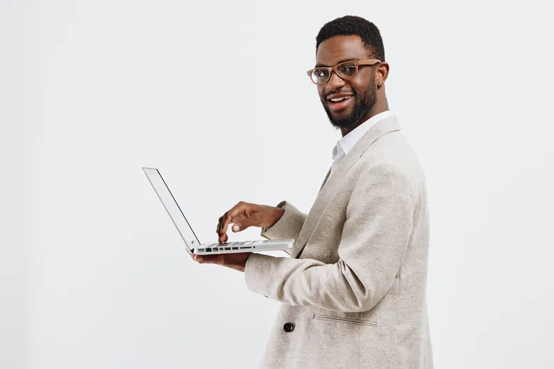 Smiling man holding a laptop, dressed in a beige blazer and white shirt, looking at camera on plain white background, studio portrait. Business technology concept, modern professional, freelance work,