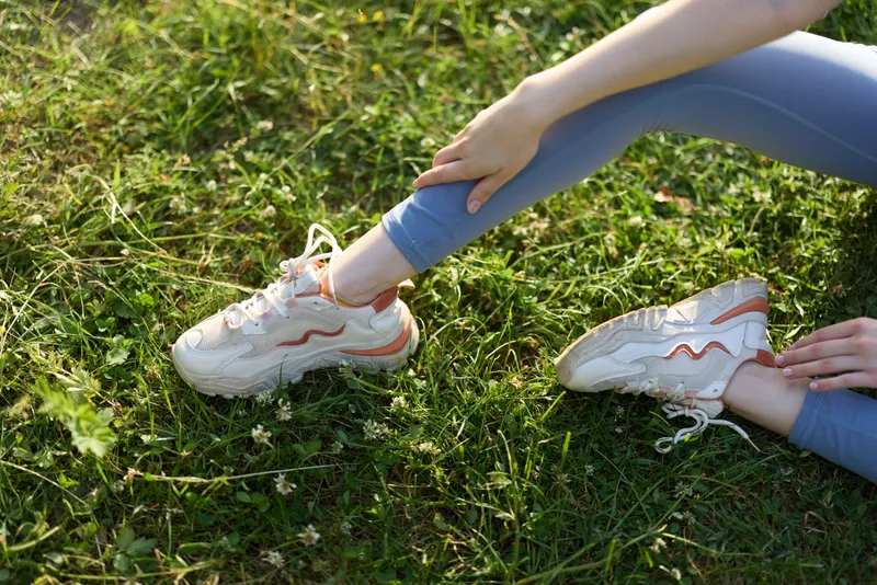 Young woman in comfortable sportswear stretching in grass wearing trendy sneakers, evoking a sense of fitness and outdoor activity