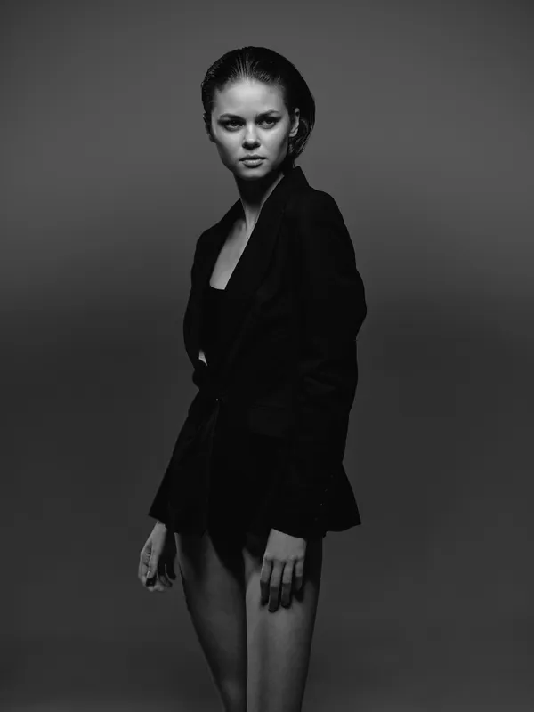 Black and white portrait of serious woman in dark blazer with slicked-back hair and minimal makeup