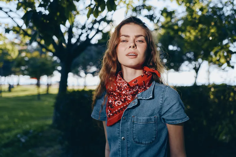 lifestyle woman in modern boho-western denim street style wearing a red bandana, natural light, film color tones, outdoor park setting, casual and relaxed vibe