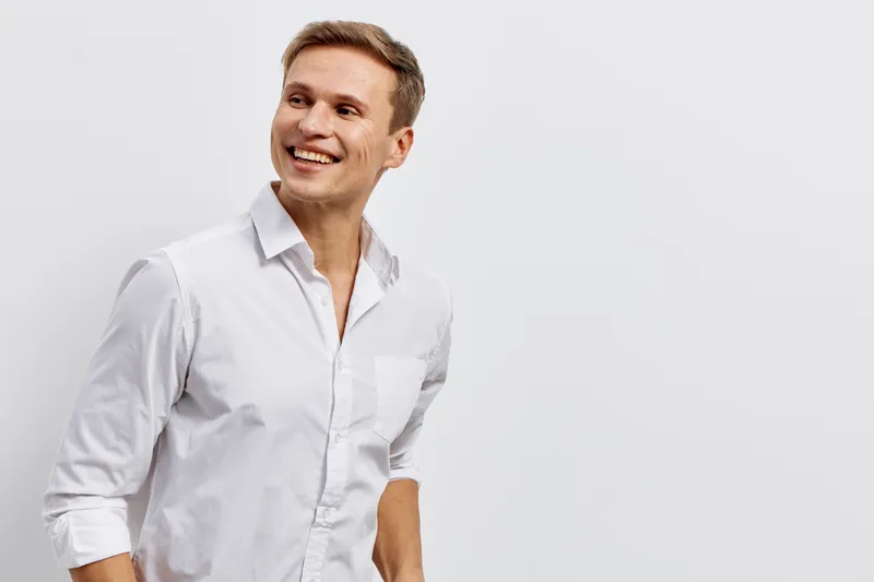 Smiling man in white shirt looking away with confident expression, casual pose, isolated on plain gray background, studio portrait, positive vibe, lifestyle concept, light professional style.