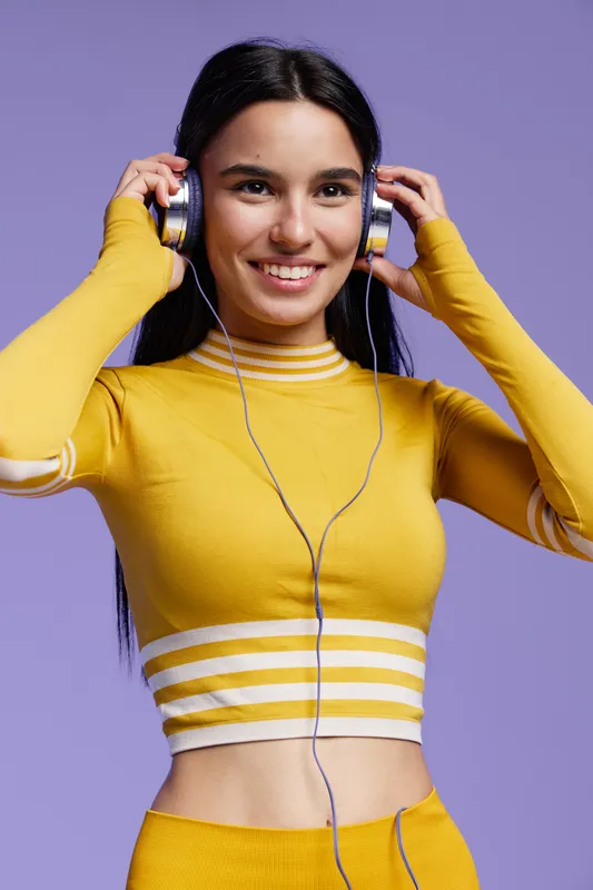 woman sport fitness wearing yellow athletic outfit with headphones smiling, posing against purple background, young adult, health and active lifestyle concept