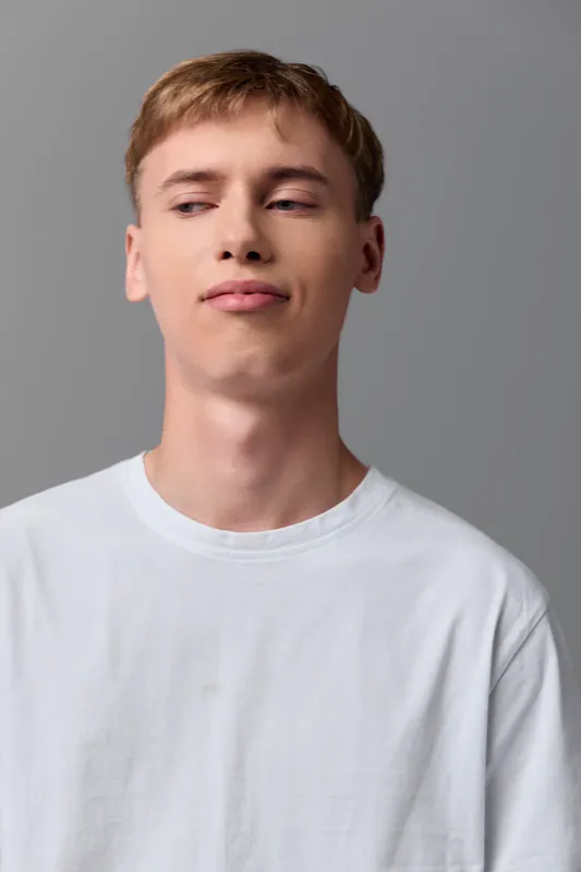Man in casual white shirt stands in a studio with calm expression, neutral background and soft lighting, creating a clean headshot for stock use