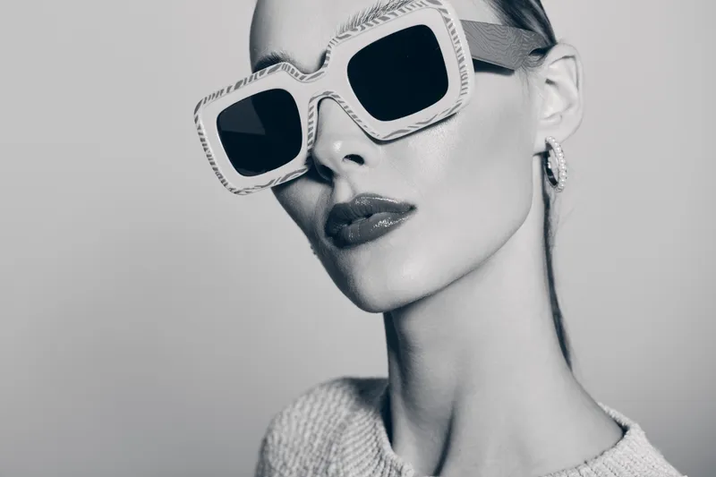 Stylish white woman with pale skin wears large square sunglasses and hoop earrings in studio. Concept of fashion accessories and modern minimalism.