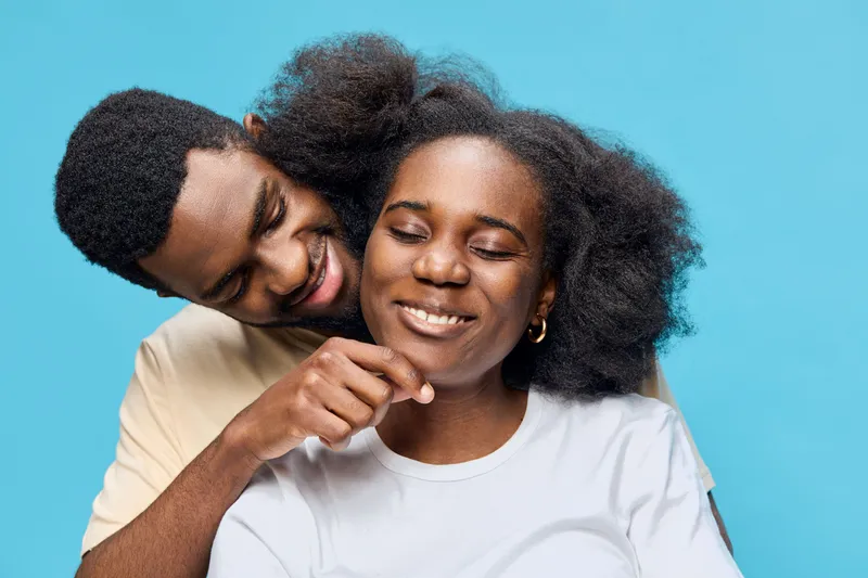 Happy couple embracing with joyful expressions, showcasing love and connection against a bright blue background, emphasizing their warmth and affection