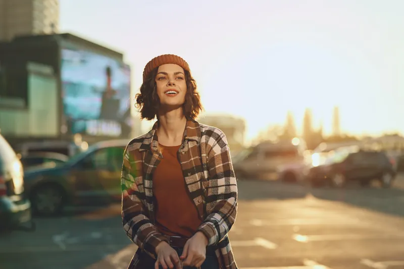 Woman portrait smile in urban parking at golden hour, candid moment with beanie and plaid coat, authenticity and lifestyle vibe, mindful living and emotional storytelling in warm glow