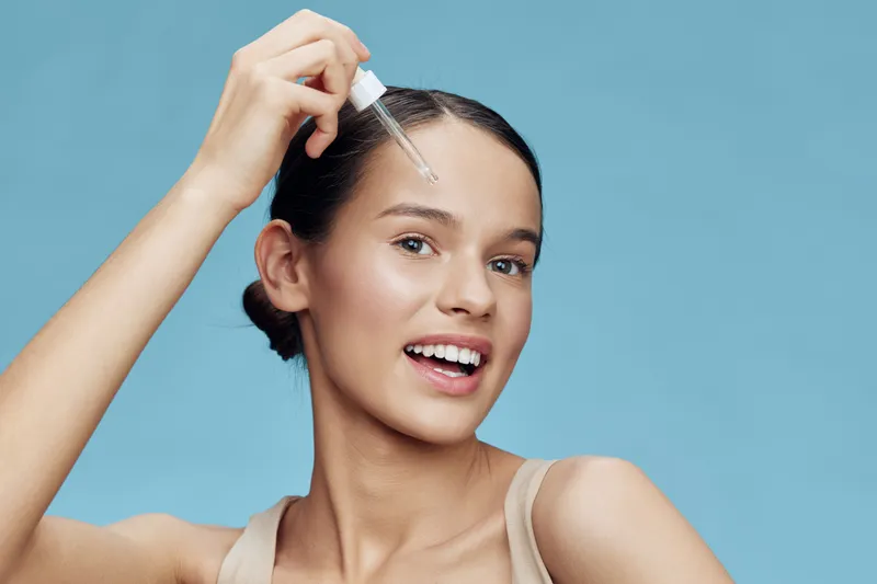 Young woman applying serum for radiant skin on a blue background, showcasing confidence and beauty in skincare