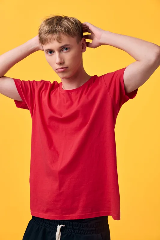 Young male model in a red shirt poses against a bright yellow backdrop, casual style and confident stance, fashion image for youth apparel, studio shoot, vibrant color contrast and clean composition