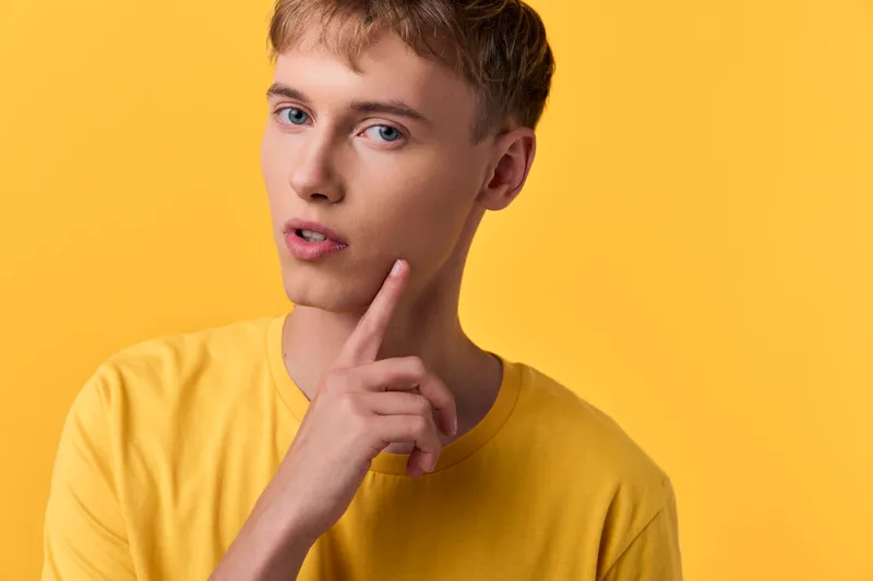 Thinking, contemplation and a pensive expression in a closeup of a young male in a yellow shirt, studio setting, calm mood, thoughtful pose, modern stock image for ideas, design concepts and creative