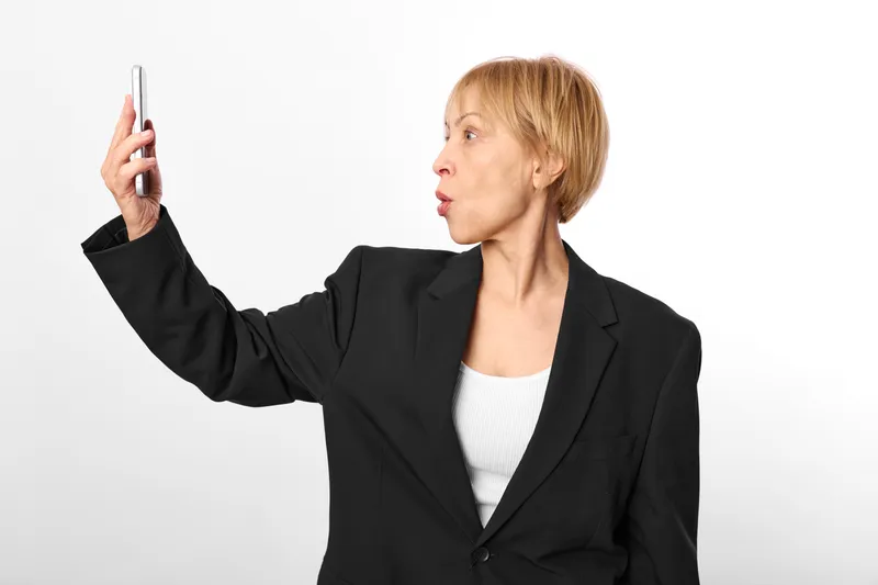 Woman businesswoman smartphone in hand pointing gesture, focused expression, modern blazer suit, explaining message, isolated on white background, side view portrait, copy space