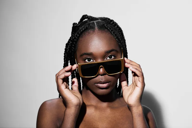Stylish female model with braided hair wearing oversized sunglasses, showcasing confidence and elegance against a minimalist background