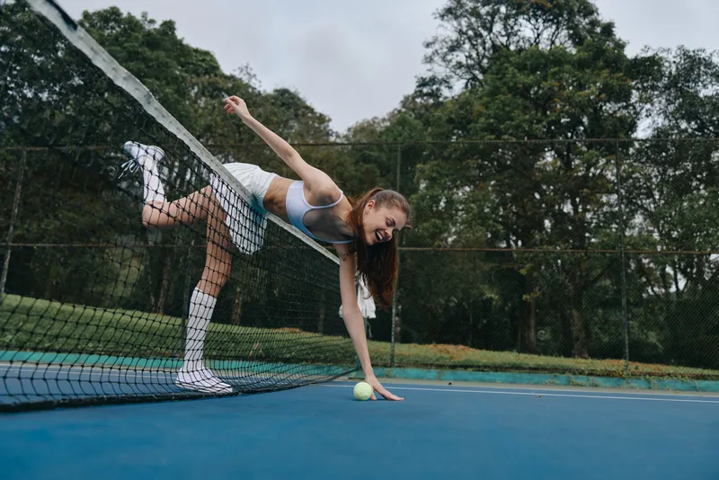 Young athletic woman enjoying tennis on a sunny day, wearing a sports outfit, showing determination while reaching for the ball on the court