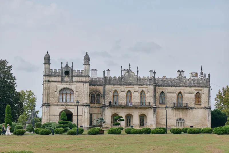 Castle and historic stone architecture rise with decorative battlements, set on a well kept lawn, surrounded by trees, capturing medieval heritage in a tranquil landscape.
