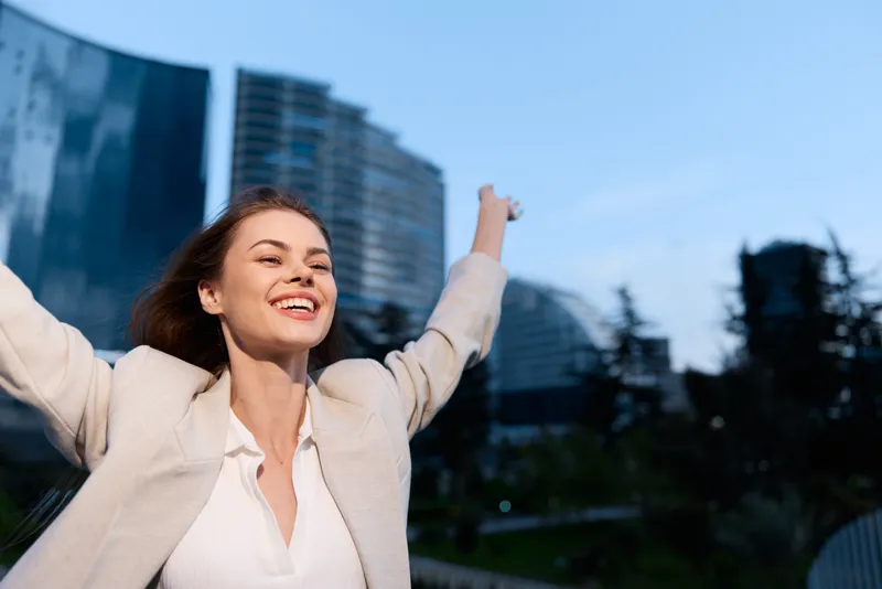 Confident businesswoman celebrating success in an urban setting, wearing a stylish blazer and expressing joy against a modern city skyline.