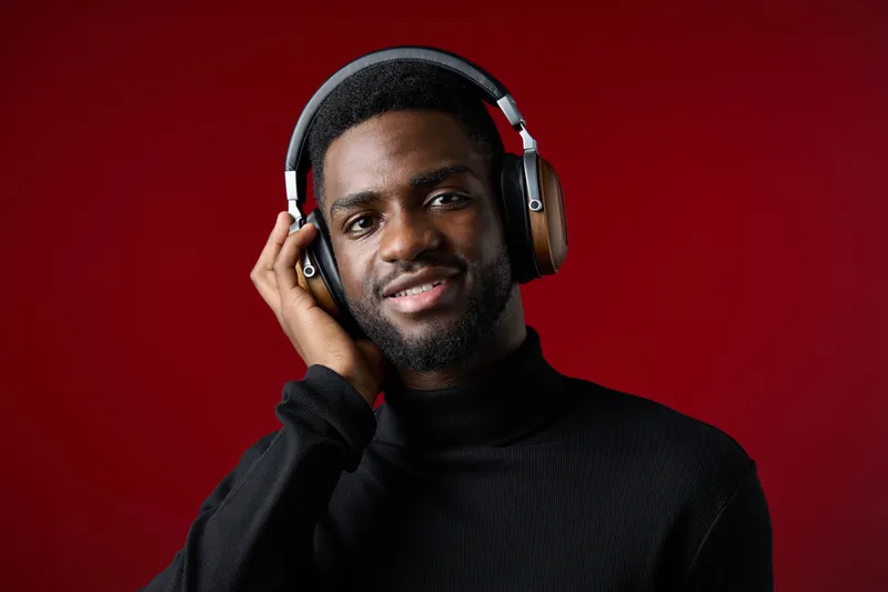 Young Black man wearing headphones and smiling while listening to music against a vibrant red background, showcasing joy and modern lifestyle