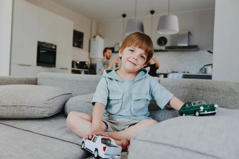 Happy boy playing with toy cars in a cozy living room filled with natural light and warm colors. A playful atmosphere promotes imagination and creativity.