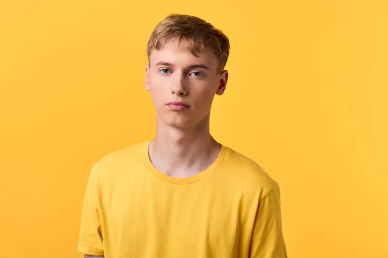 Young man in a yellow shirt stands before a bright background in a studio, casual fashion and minimal clean composition with soft lighting and modern lifestyle vibe