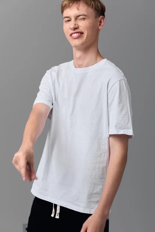 Man in a white t shirt extends his arm with a confident gesture in a clean studio setting, highlighting casual wear, relaxed mood, and contemporary fashion for lifestyle or apparel showcases