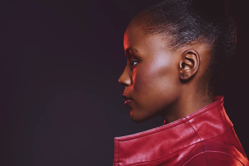Profile of a young black woman with dark skin wearing a red leather jacket against a dark background. Concept of fashion, beauty, confidence, and modern style.
