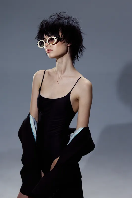slender woman in black dress with sunglasses posing against gray background stylish elegant look