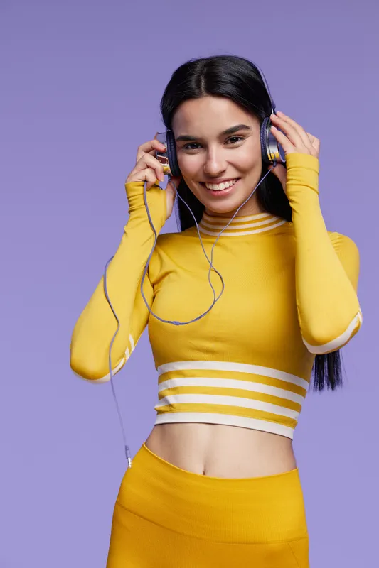 Young woman sport fitness wearing yellow activewear smiling with headphones, energetic and healthy lifestyle, purple background, joy and motivation.