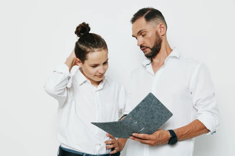A professional man and colleague study a document on an isolated colored background, conveying business focus, calm emotion, and confident teamwork in a clean, modern scene.