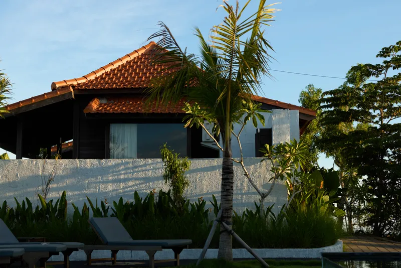 Bright tropical villa with palm trees, white wall, and shaded seating by lounge chairs. Outdoor lifestyle scene suggesting relaxation, vacation, and leisure in a sunny resort setting calm.