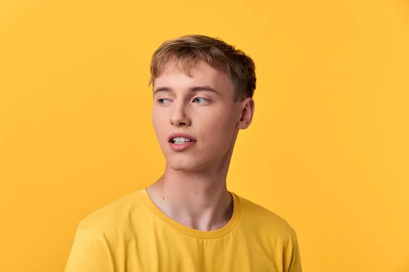 Young man in a yellow shirt against a bright yellow background, casual pose and thoughtful expression, clean studio shot, lifestyle and fashion vibe, cheerful mood.