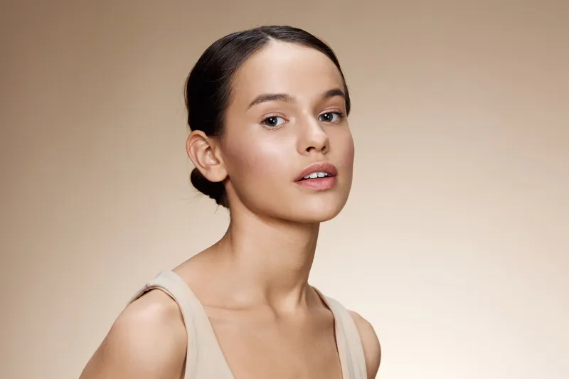 Young woman with natural makeup and neutral attire, exuding confidence and serenity against a soft, beige background Ideal for beauty and skincare concepts