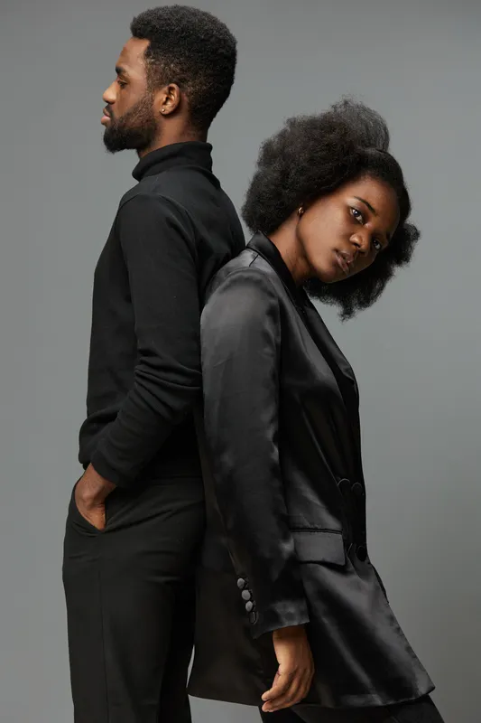 Elegant couple in stylish black outfits, showcasing confidence and emotion against a neutral background, perfect for themes of modern romance and fashion