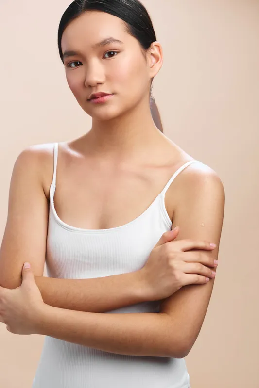 Asian woman stands with crossed arms in a simple studio setting, calm and confident, conveying a thoughtful mood ideal for wellness, fashion, or lifestyle projects seeking a contemporary,