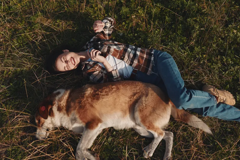 Woman lying on grass with a dog outdoors, enjoying companionship and relaxation in nature, a casual portrait of bond and calm in the open air.
