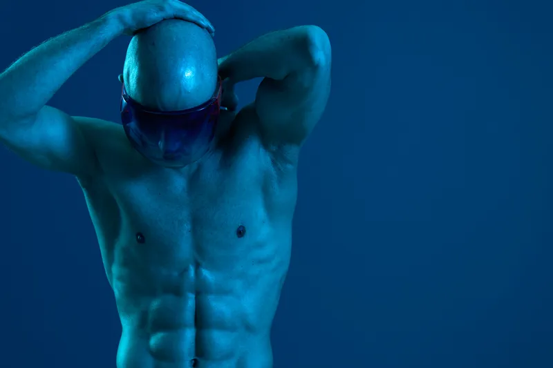 Athletic man posing in a dynamic stance, showcasing strong physique and vibrant blue lighting. The image emphasizes strength and determination, with an artistic flair.
