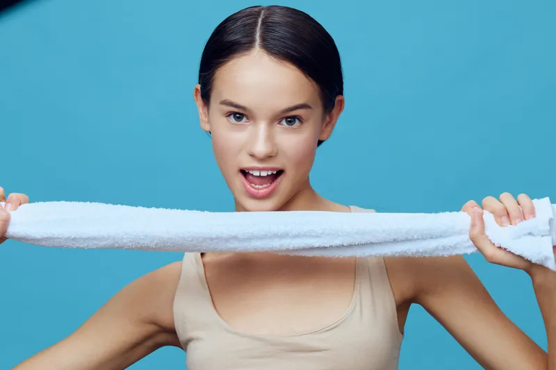 Young female model with a towel demonstrating joy and fitness in a light blue background showcasing healthy lifestyle, emotion, and sportswear