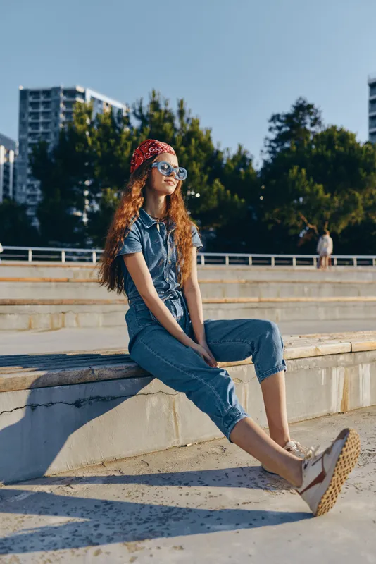 Lifestyle woman in modern boho-western denim street style relaxing outdoors in sunny urban setting with film color tones and casual summer vibe