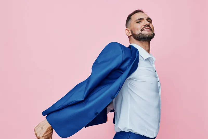 A professional man in a blue suit strikes a dynamic pose against a solid pink background, conveying confidence, focus, and energetic business style and mood.