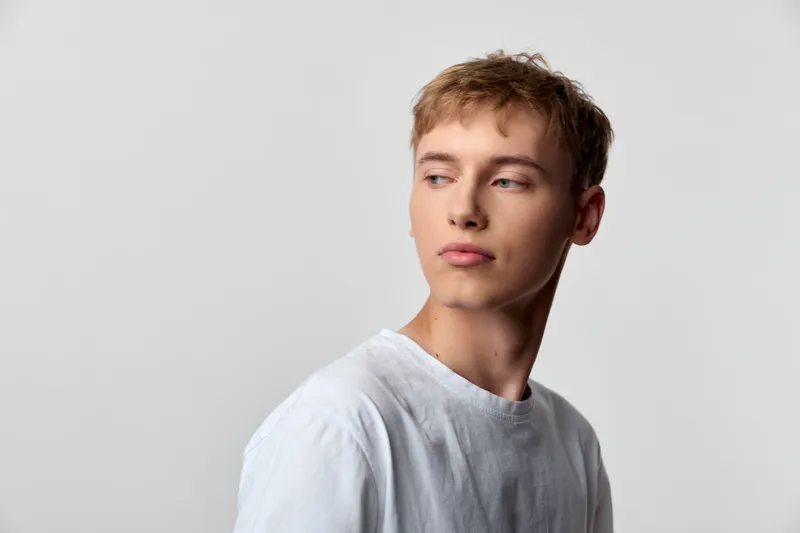 Man, youth, tshirt, sideview pose with calm gaze in a soft studio setting, minimal background, fashion style and expressive mood suitable for creative projects and stock use