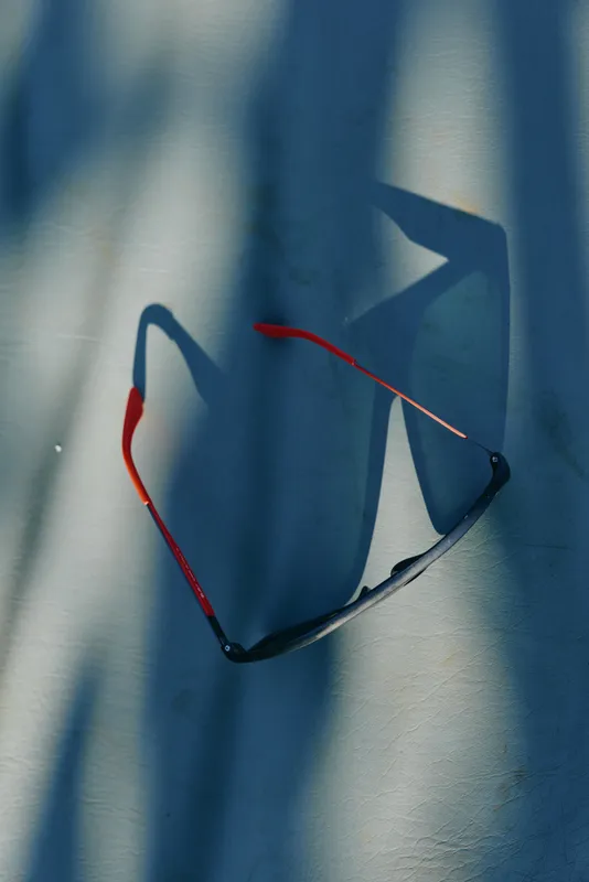 Sunglasses hang on a blue background, casting dramatic shadows, highlighting frame and lens, a casual fashion accessory in an urban lifestyle scene with moody light glow