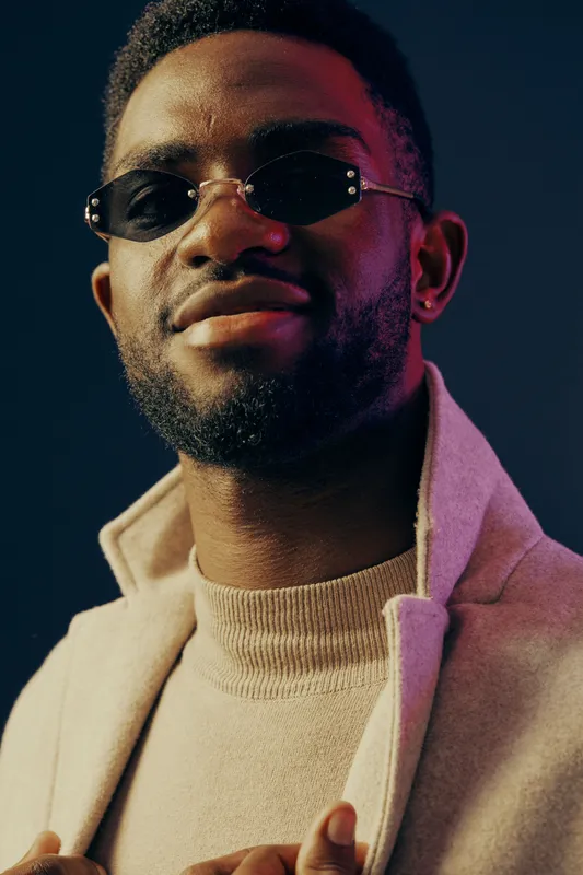 Confident young Black man in stylish sunglasses and a cozy sweater against a colorful background, embodying modern fashion trends and self assurance