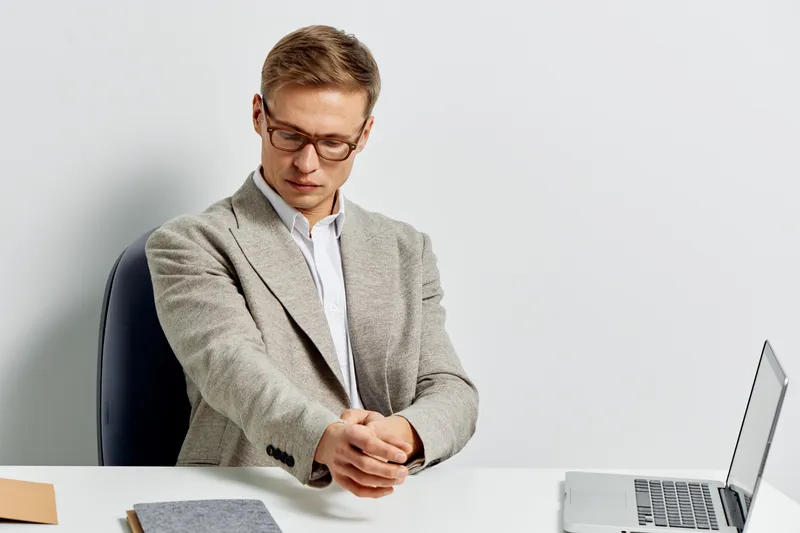 young man stretching hands in casual blazer sitting at desk with laptop and notebook digital nomad concept work in metaverse