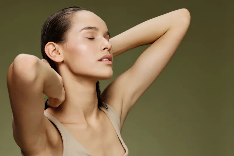 Young woman with a serene expression, showcasing natural beauty against a soft green background in minimalist attire, emphasizing wellness and self care