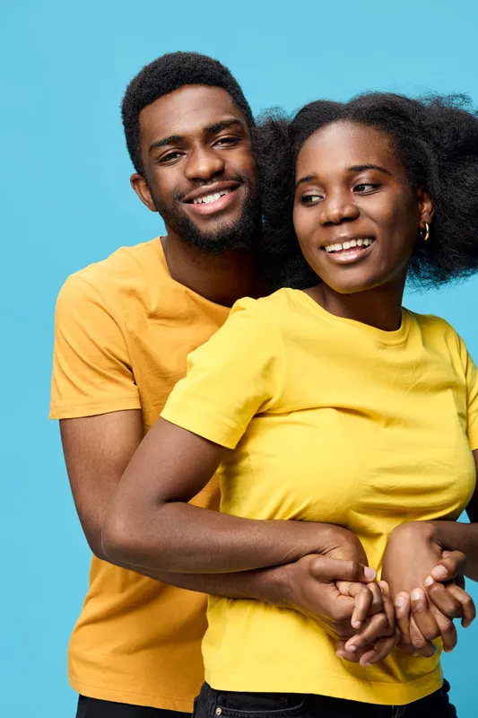 Happy young couple in matching yellow and orange shirts, smiling against a bright blue background, representing love and togetherness in a vibrant lifestyle concept