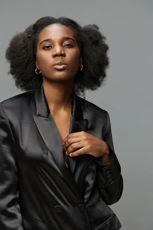 Stylish young African American woman in a satin blazer showcasing natural beauty and confidence against a muted background, ideal for fashion and empowerment themes