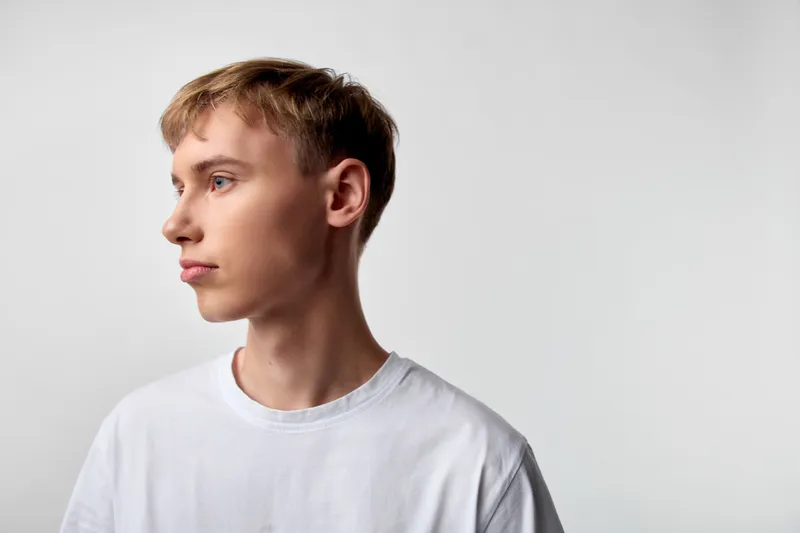 Man in white shirt gazes to the left against a neutral studio backdrop, conveying calm focus and contemplation, minimal lighting, clean composition, reflective mood, modern style without branding