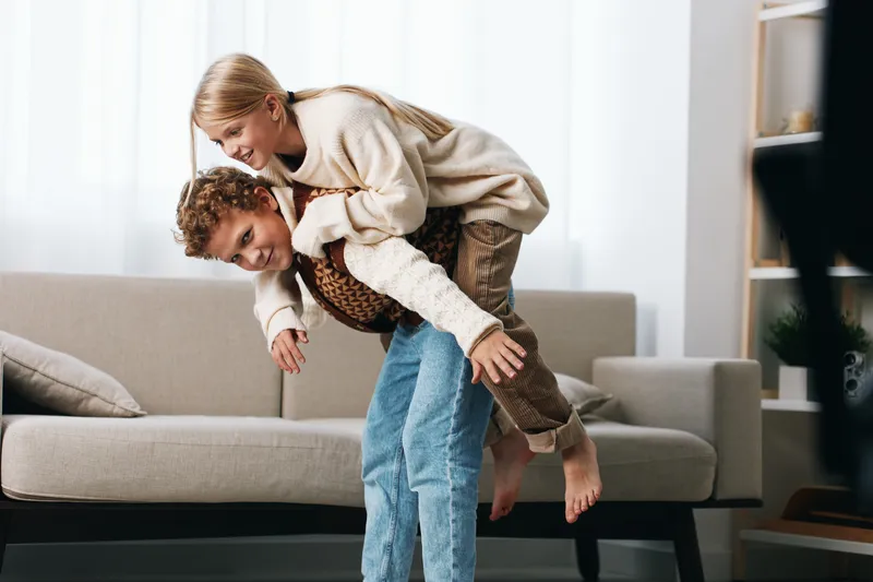 Joyful couple shares a playful piggyback moment in a cozy living room, capturing laughter, connection, and carefree energy between partners.