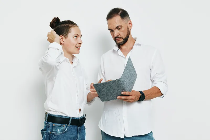 Two professionals, a man and a colleague, discuss a project with confident, focused energy as they review a document against an isolated color background.