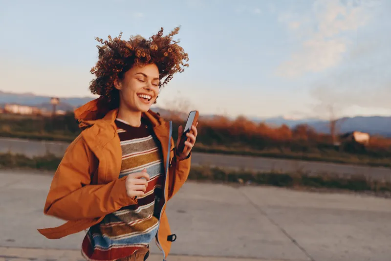 woman lifestyle outdoors autumn smile jacket street peace waving curly hair afro American woman walking sidewalk at sunset, peace sign hand gesture, warm orange jacket, relaxed cheerful mood