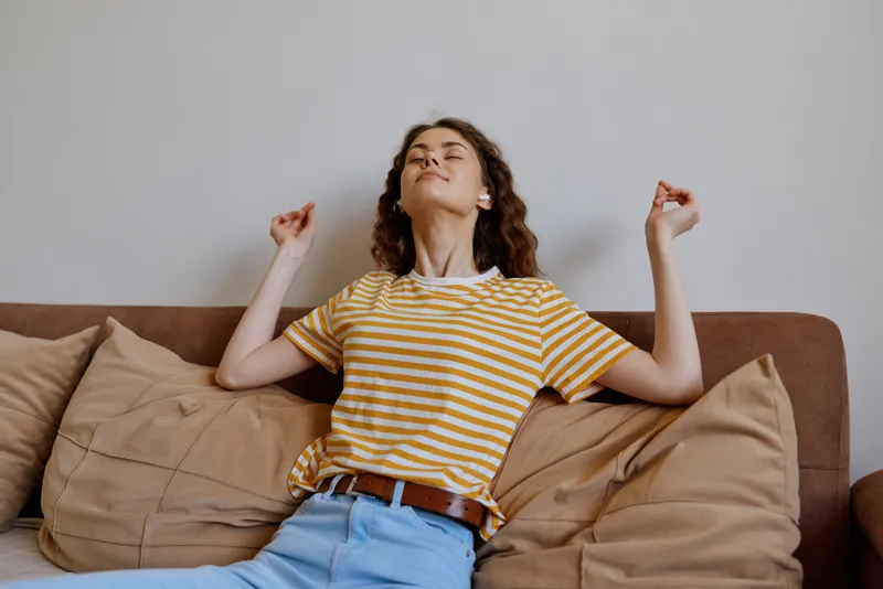 Relaxed woman at home lounging on a sofa, wearing a striped tee and jeans, enjoying a casual moment in a cozy living room bathed in soft natural light and peaceful mood.