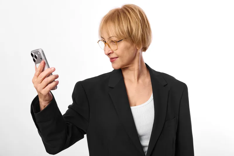 Senior woman smartphone business suit glasses technology communication, smiling and looking at the screen, isolated on white background, portrait concept.